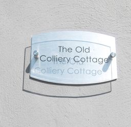 A sign on a textured wall displaying The Old Colliery Cottage at Old Colliery Cottage in Shilbottle