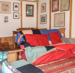 A living room with a sofa covered by colorful blankets and cushions a wooden table and chairs framed pictures on the wall at Can Yr Afon in Beddgelert