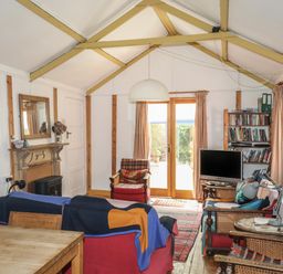 A living room with red armchairs a wooden table a TV on a stand bookshelves and double doors with curtains at Can Yr Afon in Beddgelert