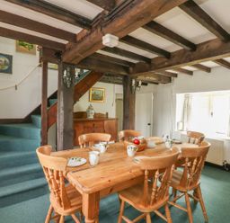 A dining area with wooden table and chairs near stairs and window at Thatch Cottage in Buckland Newton