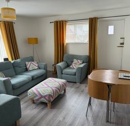 A living room with two sofas an armchair an ottoman a dining table and chairs a floor lamp and a wall-mounted television at The Old Coach House in Conwy