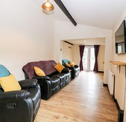 A living room with black recliner sofas yellow and blue cushions and a wall mounted television at Squirrel Lodge in North Walsham