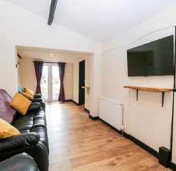 A living room with black leather sofas yellow pillows mounted television and wooden floor at Squirrel Lodge in North Walsham