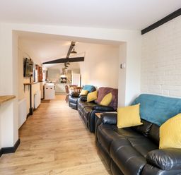 A living room with black leather sofas and yellow cushions leading to a kitchen and dining area at Squirrel Lodge in North Walsham