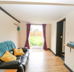 A sitting room with a black sofa yellow cushions and an open door leading to a garden at Squirrel Lodge in North Walsham