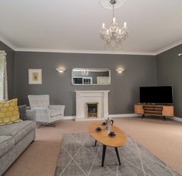 A living room with a sofa chairs a coffee table a fireplace a TV on a stand and windows at Cherry Tree House in Highbridge