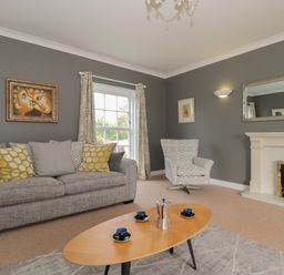 A living room with a gray sofa and patterned cushions a coffee table with cups and a coffee maker an armchair a fireplace and wall art at Cherry Tree House in Highbridge