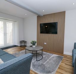 A sitting room with two blue sofas a round coffee table a wall-mounted TV and sliding glass doors at Riverside Cottage No 3 in Keswick