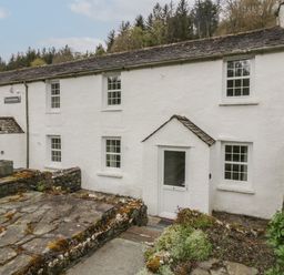 An exterior view of a white cottage with a stone roof and multiple windows at Riverside Cottage No 5 in Keswick
