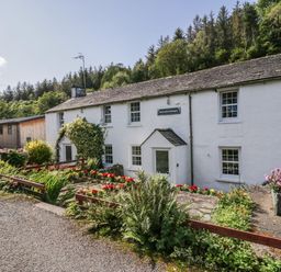A white cottage with multiple windows and a garden with flowers and greenery at Riverside Cottage No 5 in Keswick