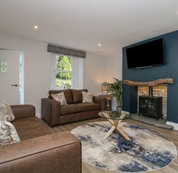 A living room with brown sofas a round rug and a television above a fireplace at Garden Cottage No 1 in Keswick