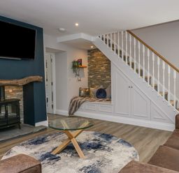 A living room with a glass coffee table on a round rug and a TV above a wood stove at Garden Cottage No 1 in Keswick