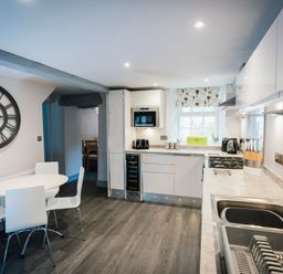 A kitchen with white cabinets a round white table with four chairs and a large wall clock at Greta House in Keswick