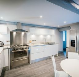 A modern kitchen with stainless steel oven and refrigerator white cabinets and a round dining table at Greta House in Keswick
