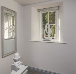 A window with a sculpture on the sill and a mirror reflecting the sculpture in a hallway at Greta House in Keswick