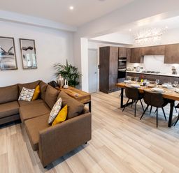 An open-plan living room and kitchen with a brown sectional sofa and a wooden dining table at Briery House in Keswick