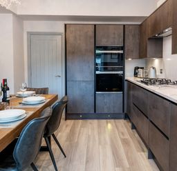 A kitchen with wooden dining table set with plates and glasses and dark cabinets with built in ovens at Briery House in Keswick