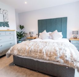 A bedroom with a bed with fur blanket two bedside tables with lamps a chest of drawers a plant and a decorative mirror at Briery House in Keswick
