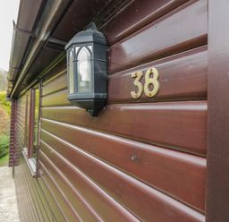 Outdoor wall of a brown wooden cabin with a black lantern and number 38 in Keswick