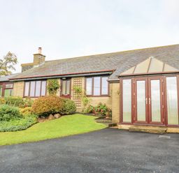 A single-story house with stone walls and a slate roof with a paved driveway and shrubs at Pinegarth in Catton near Allendale