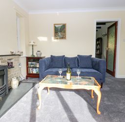 A living room with a blue sofa and a glass coffee table with a bottle and glasses at Pinegarth in Catton near Allendale