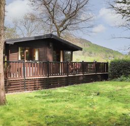 A wooden cabin with a fenced porch surrounded by grass and trees at Derwent Lodge in Keswick