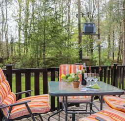 An outdoor wooden deck with a glass table and four striped cushioned chairs surrounded by trees at Derwent Lodge in Keswick