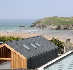 A beach with people walking near the sea and rocky green hill in the background viewed from houses at 11 Ebbtide in Porth