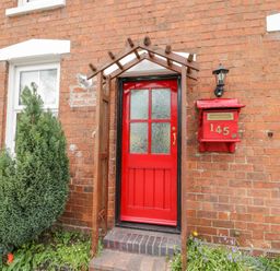 A red door with a red mailbox numbered 145 on a brick house exterior at Dobbies Den in Bewdley