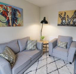 A living room with grey sofa and armchair a floor lamp and paintings of an elephant and donkeys at Dobbies Den in Bewdley