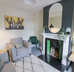 A living room with a gray armchair and sofa a fireplace with a mirror and plants and a painting of three donkeys at Dobbies Den in Bewdley