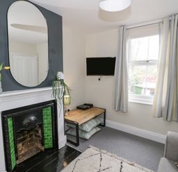 A living room with a fireplace a wall mirror TV on a wall and a window at Dobbies Den in Bewdley
