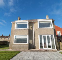 The exterior of a two-story house with large windows and a paved patio at Fairwinds in Newbiggin-By-The-Sea