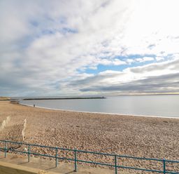 A sandy beach with a blue railing and a calm sea at Fairwinds in Newbiggin-By-The-Sea