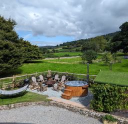 An outdoor area with a hot tub wooden chairs a hammock and a green roofed shed in a grassy field at Ty Sinsir in Tretower