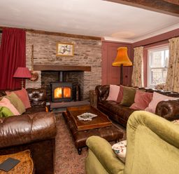 A living room with leather sofas a green armchair a wood burning stove and cushions at Ty Sinsir in Tretower