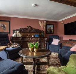 A living room with blue and green armchairs a carved wooden desk wooden coffee table and paintings on pink walls at Ty Sinsir in Tretower