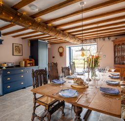 A dining area with a wooden table set with plates glassware and candles and blue kitchen cabinets in the background at Ty Sinsir in Tretower