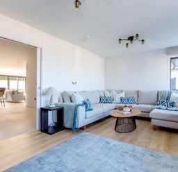 A living room with a beige sectional sofa and blue patterned cushions at 12 Tintagel Terrace in Port Isaac
