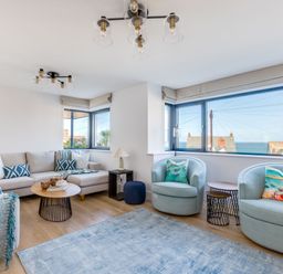 A living room with a beige sectional sofa and blue armchairs near windows showing a sea view at 12 Tintagel Terrace in Port Isaac