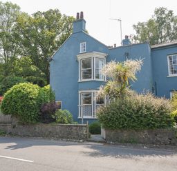 A blue house with bay windows and a garden with bushes and a stone wall at Braeside in Lyme Regis