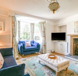A living room with blue sofas and a tufted ottoman in front of a fireplace at Braeside in Lyme Regis