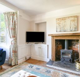 A living room with a wood burning stove fireplace television floral curtains and a blue armchair at Braeside in Lyme Regis