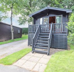 A cabin with stairs leading to a front porch surrounded by grass and trees at Ennerdale Lodge in Burnside Park near Keswick