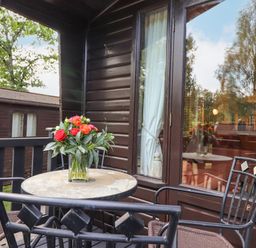 A balcony with a stone table and metal chairs with red flowers on the table at Ennerdale Lodge in Burnside Park near Keswick