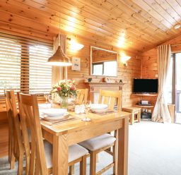 A dining area with a wooden table set with plates and glasses and a television on a corner wall at Ennerdale Lodge in Burnside Park near Keswick