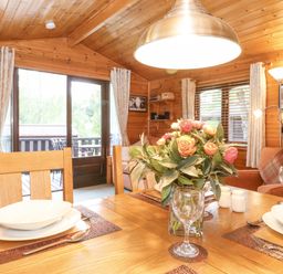 A dining area with wooden table set with plates glasses and a flower vase in a wooden cabin at Ennerdale Lodge Burnside Park near Keswick