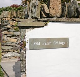 A stone wall with a metal sign reading Old Farm Cottage at Old Farm Cottage in Skelwith Fold