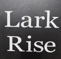 A black sign with white text that reads Lark Rise