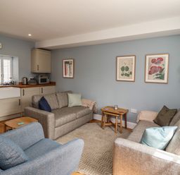 A living room with sofas, an armchair, side tables, wall art, and kitchen cabinets at Lark Rise in Alnmouth
